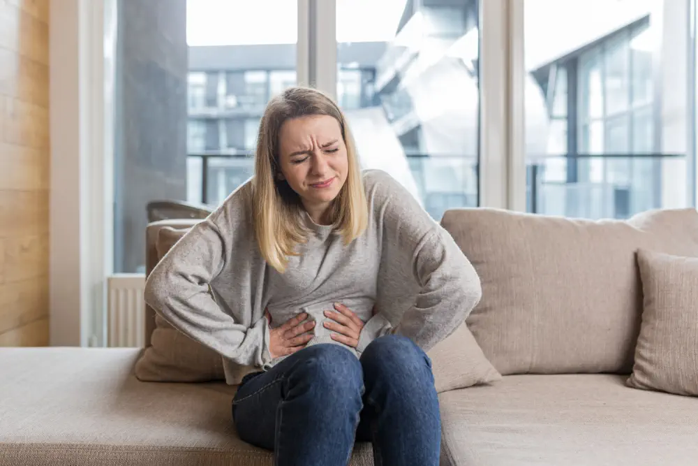 A woman sitting on a couch clutching her stomach in pain.